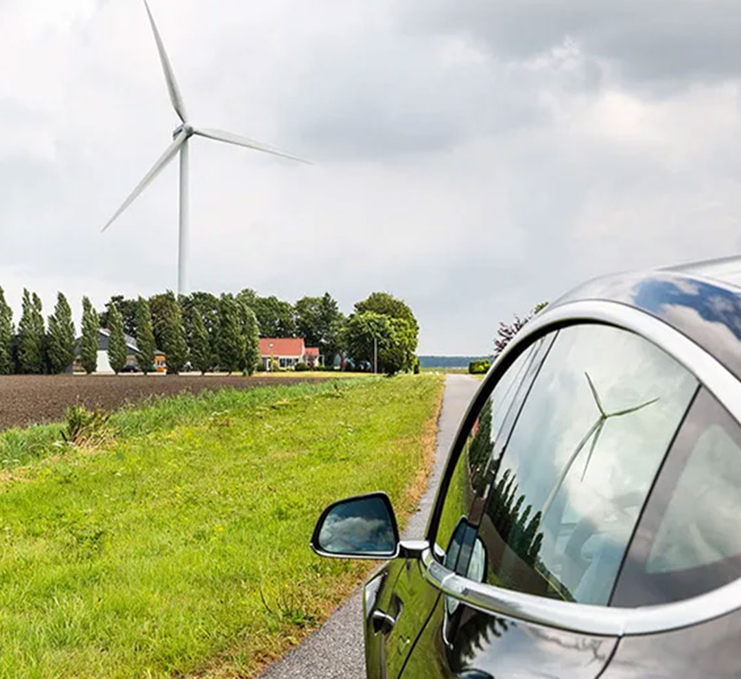 An electric car standing on a road with a windmill next to it