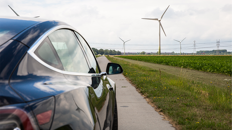 Electric car driving on street with windmills and field in background